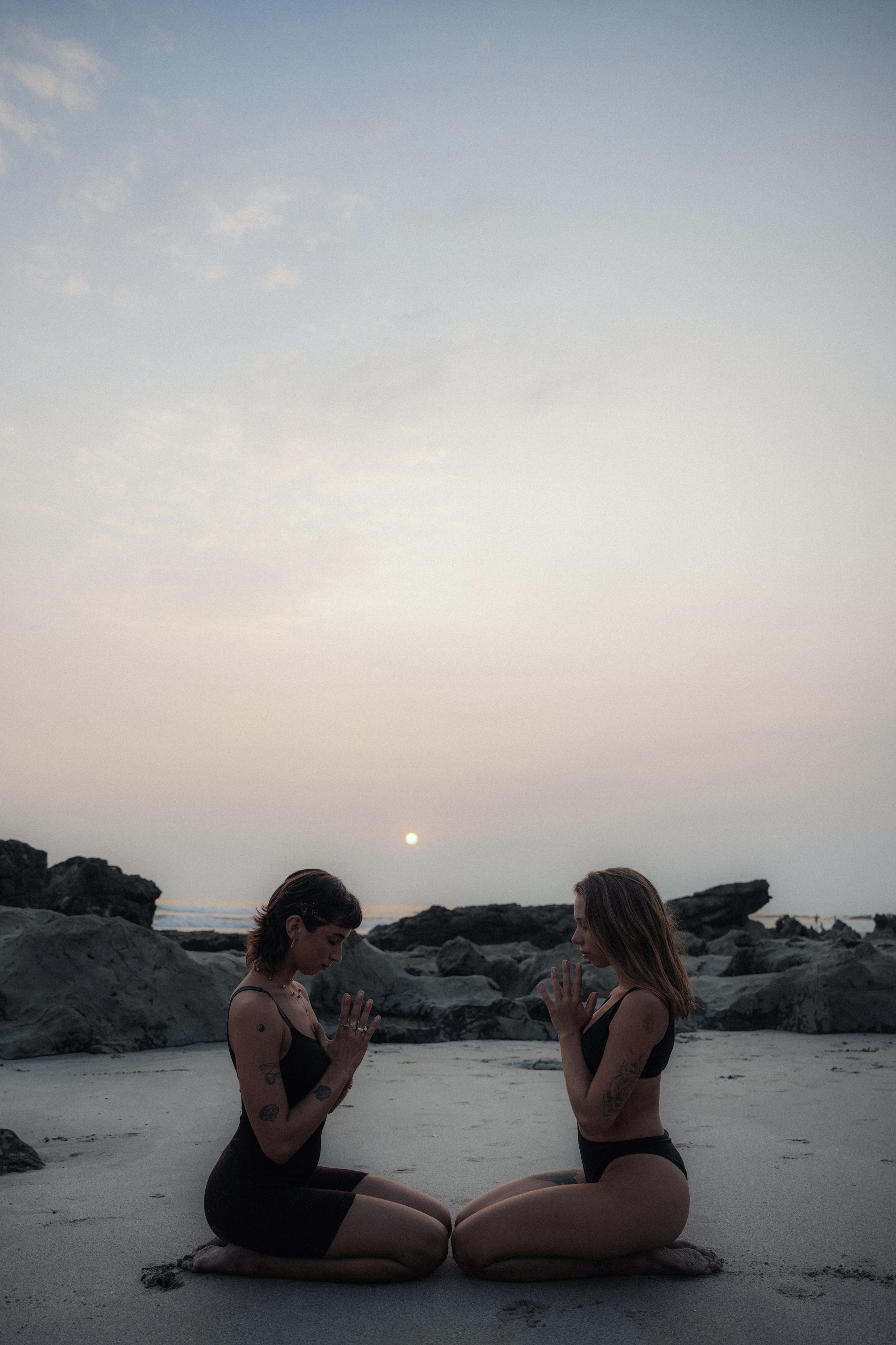 Two women kneeling in stillness on the beach at dusk